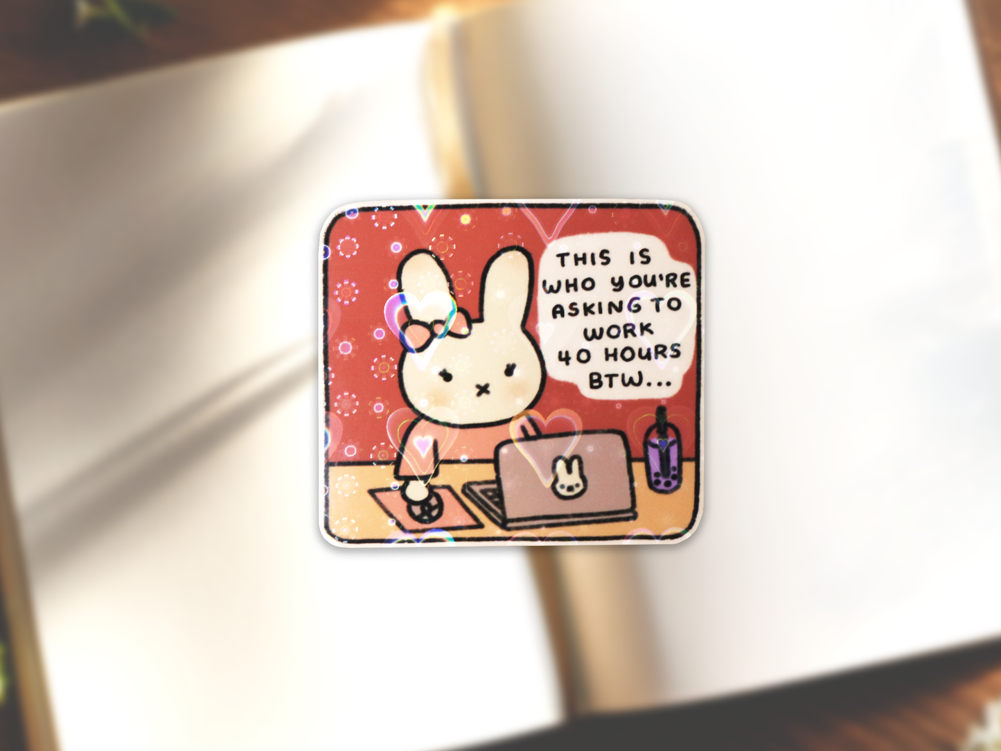Miffy bunny with a bow at a desk holding a computer mouse sticker. The desk also has a laptop with a Miffy logo and a taro bubble tea on the right side. The text reads, "This is who you're asking to work 40 hours btw..." on a dark pink background. Subtle holographic heart lamination is shown on the sticker.