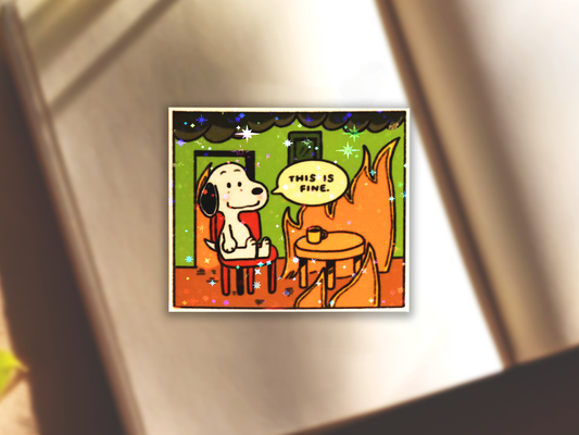 Cartoon-style illustration Snoopy sitting on a red chair and there are orange flames throughout the green room sticker. 'THIS IS FINE' is written in the speech bubble with the tail of the speech bubble leading to Snoopy's mouth. Subtle holographic star lamination shown on the sticker.